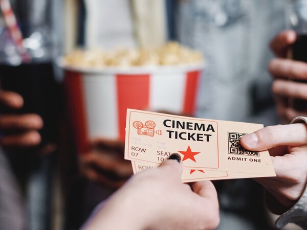 Hand holding a cinema ticket with popcorn and a soda in the background. | © Photo: @pressmaster / Freepik Licence