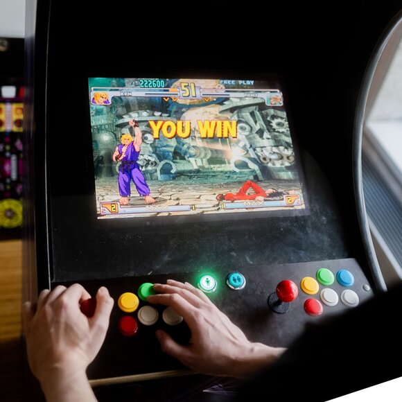 Hands of a person playing a classic fighting arcade game with 'YOU WIN' on the screen | © Photo: Ilja Kagan, 2022